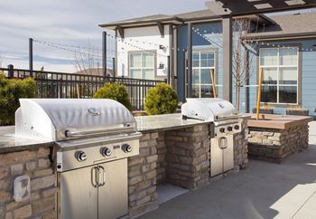 Dual outdoor barbecue grills connected by stone pavilion with stone countertops